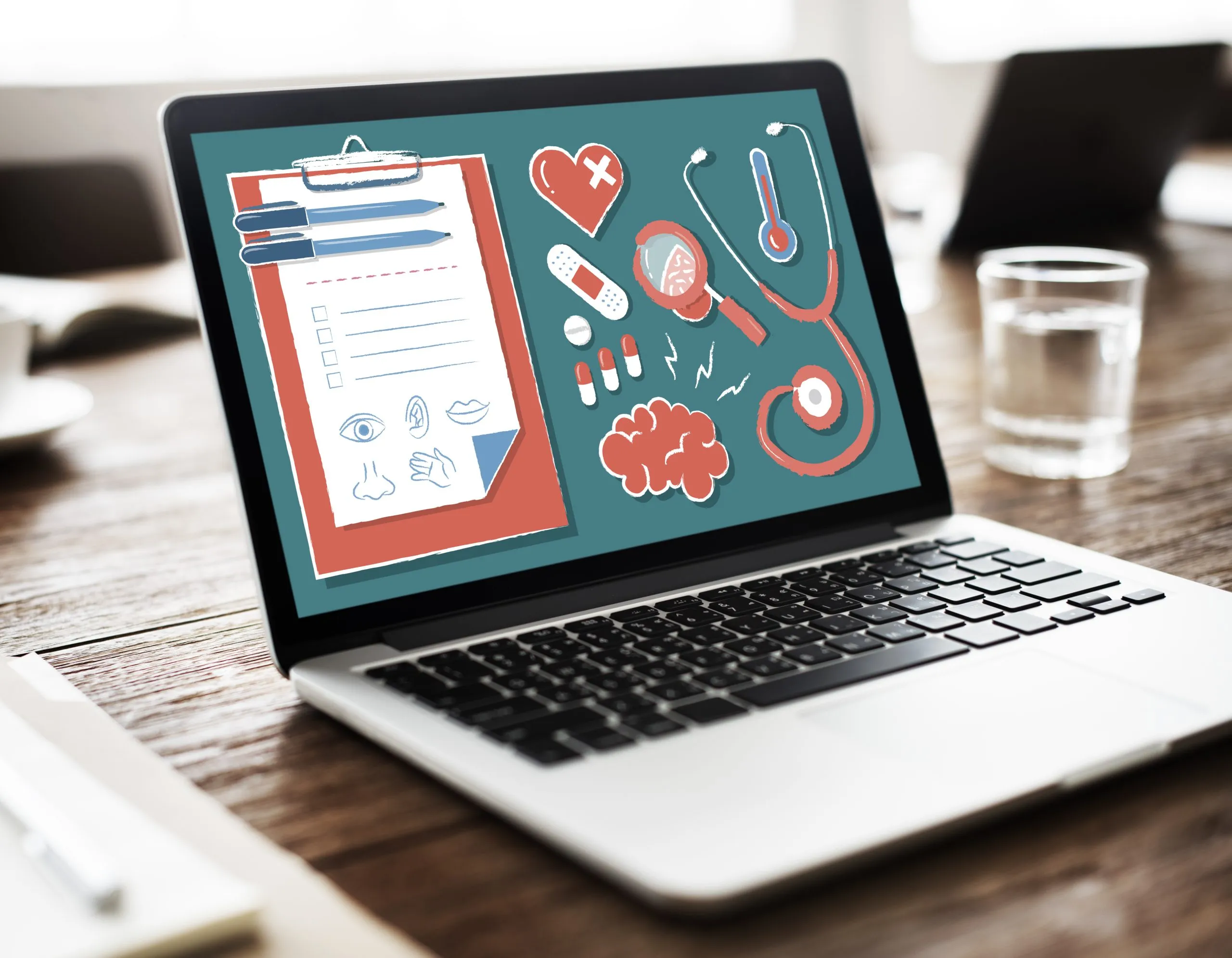 Open laptop on a wooden desk showing medical icons, a clipboard, stethoscope, heart, brain, pills, and medical tools on the screen.